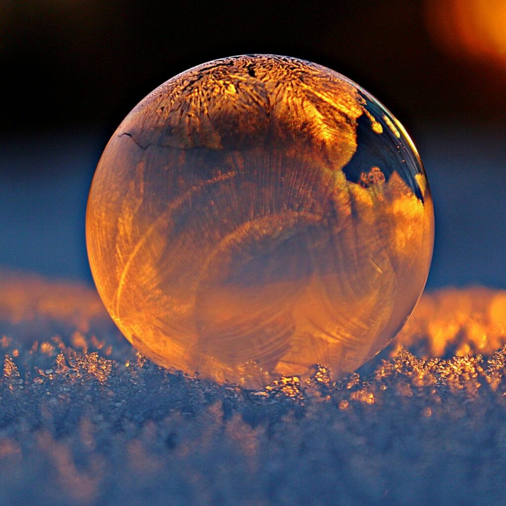 Close-up shot of a frozen bubble with warm reflections resting on a snowy surface at twilight.